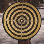 Yellow target for shooting with black circles and numbers on wooden post in countryside with snowy ground on winter day